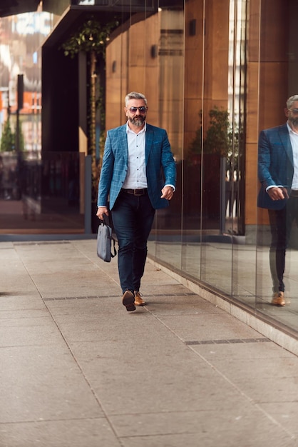 Een senior zakenman in een blauw pak met een koffer die door de stad loopt.