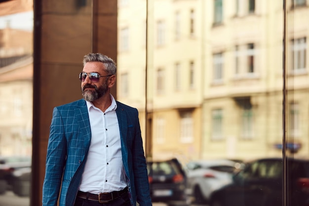 Een senior zakenman in een blauw pak met een koffer die door de stad loopt.