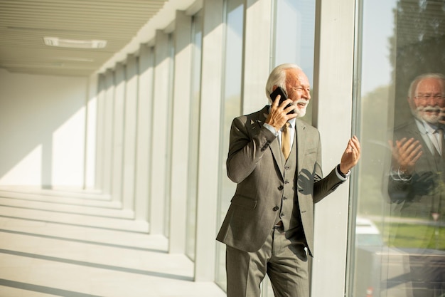 Een senior zakenman staat in een kantoorgang gefocust op zijn mobiele telefoon