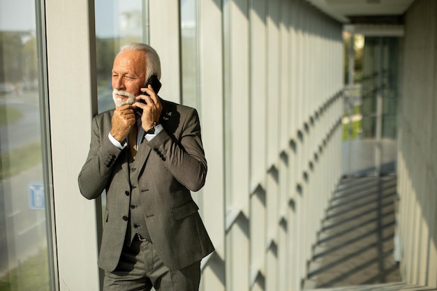 Een senior zakenman staat in een kantoorgang gefocust op zijn mobiele telefoon