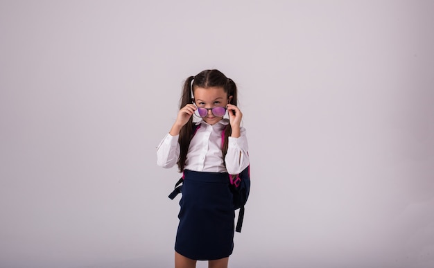 Een serieus schoolmeisje in een uniform met een bril staat op een witte achtergrond met een plek voor tekst