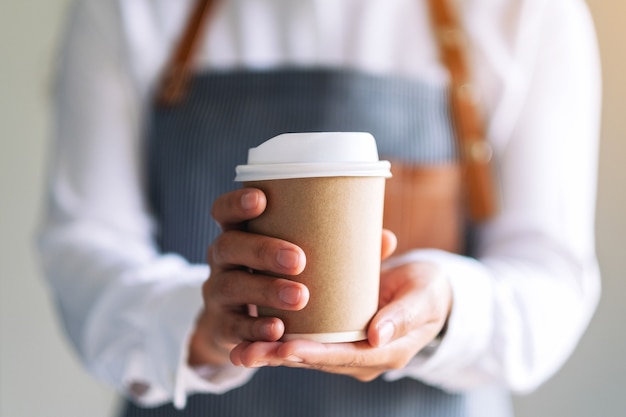 Een serveerster die een papieren kop warme koffie vasthoudt en serveert in café