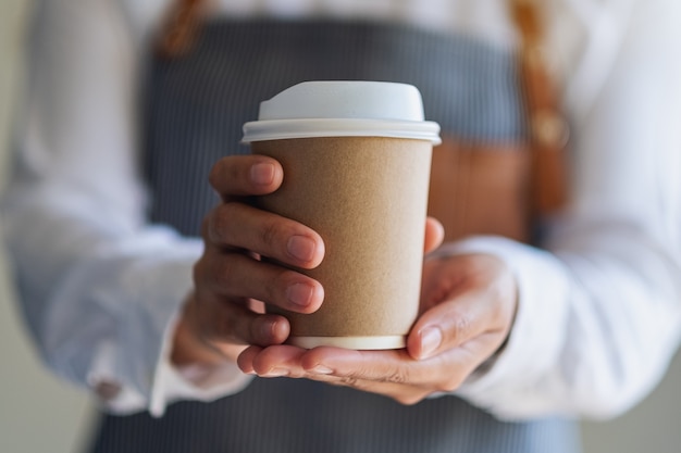 Een serveerster die een papieren kop warme koffie vasthoudt en serveert in café