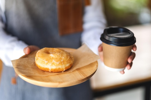 Een serveerster die een stuk zelfgemaakte donut vasthoudt en serveert in een houten dienblad en een papieren kopje koffie