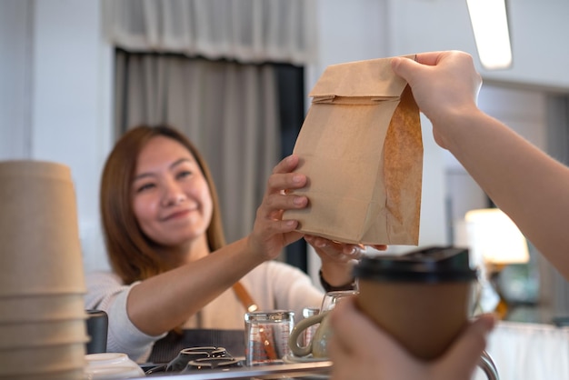 Een serveerster die koffie en een afhaalmaaltijd in een papieren zak vasthoudt en serveert aan de klant in een winkel