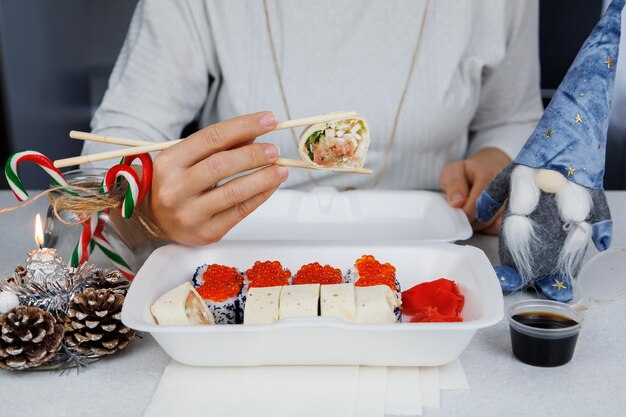 Een set Aziatische broodjes in een plastic doos thuis in de keuken in een feestelijke stijl Het meisje houdt eten vast met stokjes Kerstconcept Decoraties voor het nieuwe jaar