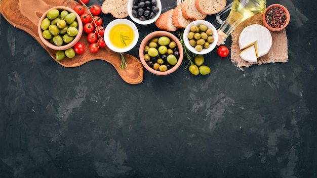 Een set groene olijven en zwarte olijven brood, kaas en kruiden Op een zwarte stenen tafel Vrije ruimte voor tekst