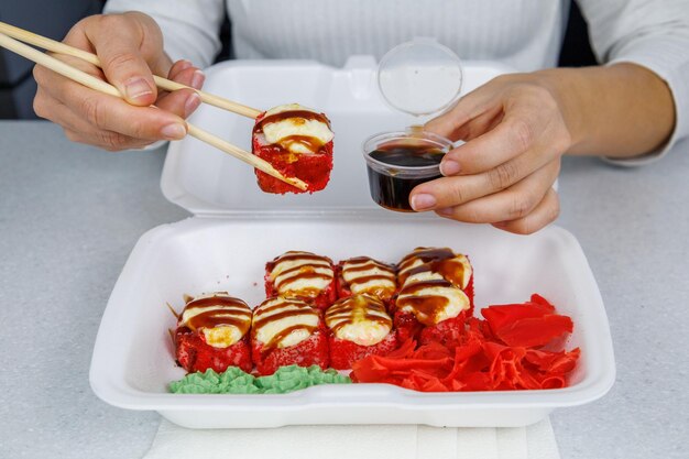 Een set japanse broodjes in een plastic doos op een lichttafel het meisje houdt eten met stokjes in haar hand snelle levering sushi in een witte container