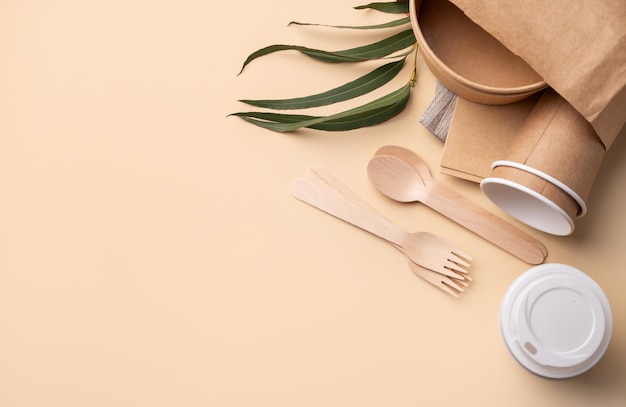 Een set milieuvriendelijk wegwerpgereedschap in een papieren zak met houten bestek, bruine papieren bekers, schalen en bamboe rietjes op groene achtergrond