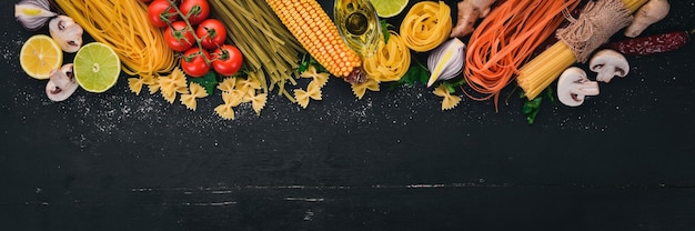 Een set van pasta noedels spaghetti tagliatelle fettuccine Farfalle Italiaans koken verse groenten en kruiden op een zwarte houten achtergrond bovenaanzicht kopie ruimte