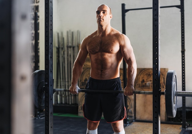 Foto een shirtloze man die een barbell tilt in de sportschool.