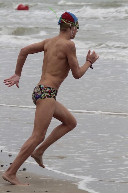 Foto een shirtloze man die op het strand loopt.