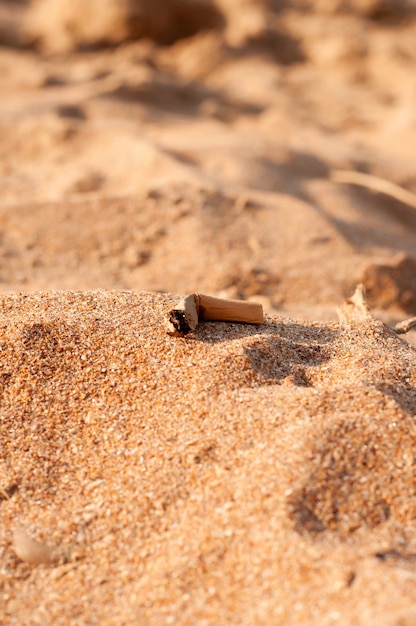 Een sigarettenpeuk ligt op het strand tegen de achtergrond van zandduinen op een wazige achtergrond