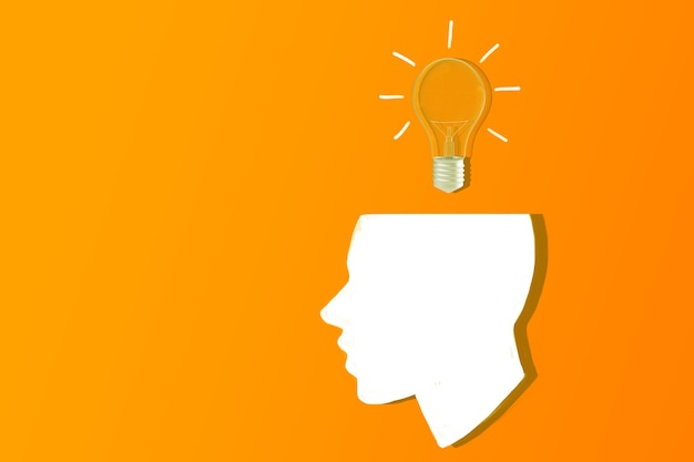Een silhouet van een menselijk hoofd met een gloeilamp bovenop op een oranje achtergrond concept van idee en creativiteit 3D Rendering