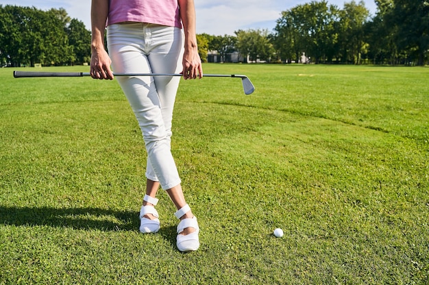 een slanke dame die met haar benen over elkaar op de golfbaan staat