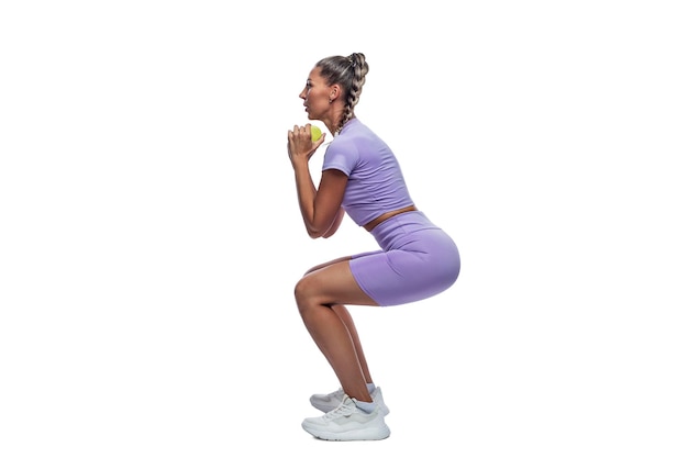 Een slanke mooie vrouw in lila sportkleding squats met dumbbells Sport gezondheid en actieve levensstijl Volledige groei Geïsoleerd op witte achtergrond Verticale zijweergave