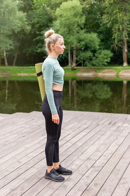 Een slanke vrouw in sportkleding die in de zomer staat met een groene gymmat om te sporten