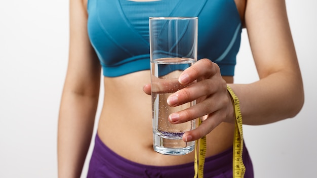 Een slanke vrouw in sportkleding houdt een glas water met een meetlint.
