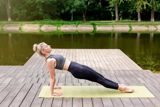 Foto een slanke vrouw op een houten platform bij een vijver in een park in de zomer doet yoga