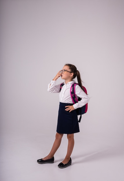 Een slim schoolmeisje in een uniform met een bril staat op een witte achtergrond met een plek voor tekst