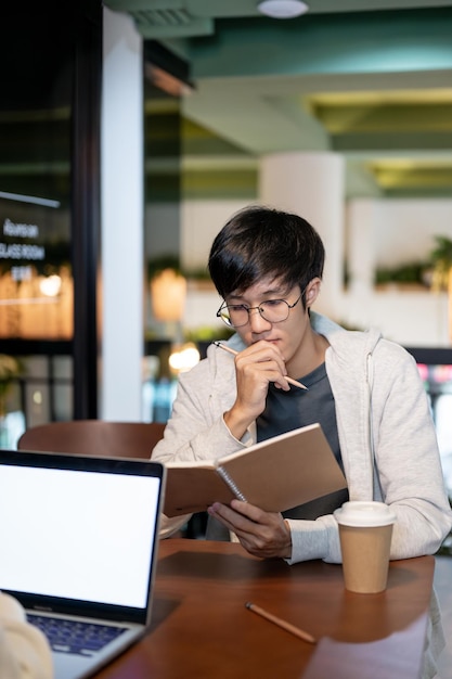 Een slimme Aziatische mannelijke student concentreert zich op het lezen van een boek om zich voor te bereiden op een examen met zijn vriend
