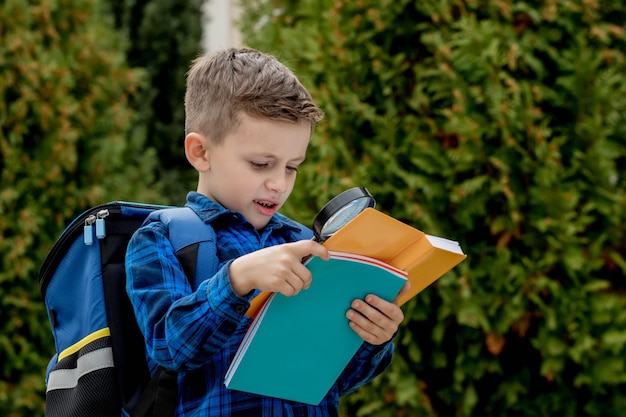 Een slimme kleine student met een vergrootglas leest een leerboek en onderzoekt nieuwe dingen