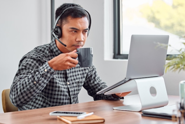 Een slokje koffie is altijd de oplossing Bijgesneden opname van een knappe jonge mannelijke callcenteragent die koffie drinkt terwijl hij op zijn laptop werkt