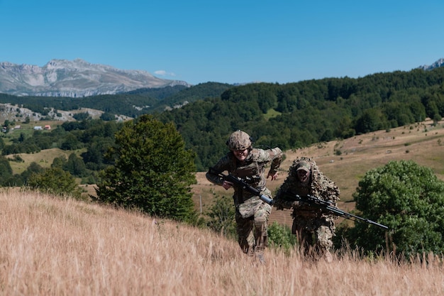 Een sluipschuttersteam van soldaten gaat undercover. Sluipschutterassistent en teamleider lopen en richten in de natuur met geel gras en blauwe lucht. Tactisch camouflage-uniform.