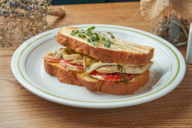 Een smakelijk en stevig ontbijt - een sandwich met kip, tomaten, witte saus en brie kaas geserveerd in een witte plaat op een houten tafel. Restaurant eten