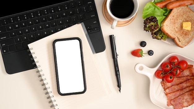 Een smartphone wit scherm op werkruimte met tabletcomputer en ontbijt of brunch. bovenaanzicht