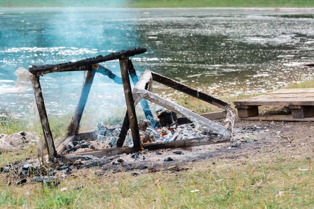 Een smeulende structuur van planken en balken op de rivieroever. afvalverbranding op het platteland. milieuvervuiling