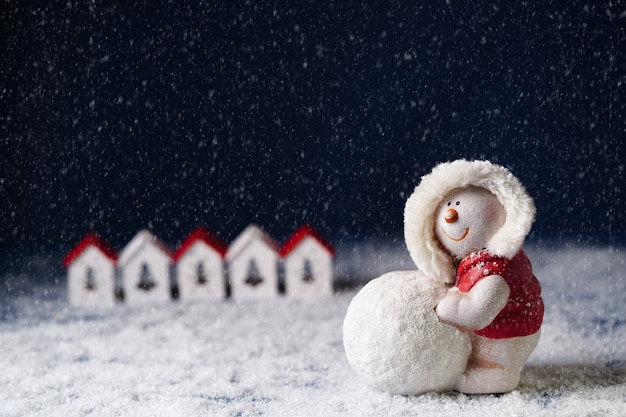 Een sneeuwpop rolt een sneeuwbal op de achtergrond van kleine huisjes op een donkerblauwe achtergrond