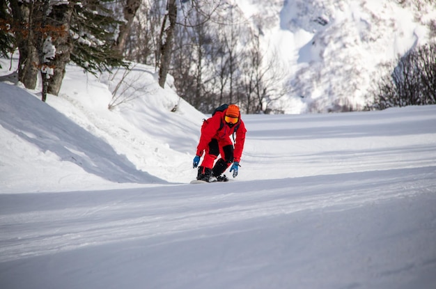 Een snowboarder in een rode jumpsuit rijdt langs een bospad in de bergen