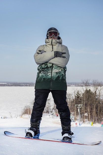 Een snowboarder staat op de top van een berg met zijn armen over elkaar Een snowboarder in moderne sportkleding en uitrusting Verticale banner