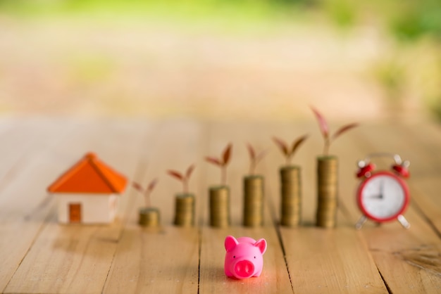 Een spaarvarken legde de stapelgouden munten en het schoolbord en de klok op de vintage blauwe achtergrond op, bespaart geld om een ​​nieuw vastgoed of lening te kopen voor geplande investeringen in het toekomstige concept.