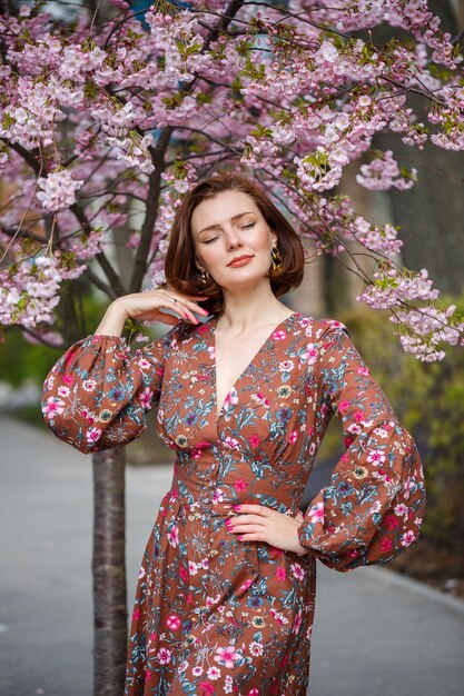 Een spectaculaire vrouw in een lichte jurk staat tegen de achtergrond van sakura. Een donkerharige vrouw in een mooie outfit lacht op straat tijdens het wandelen