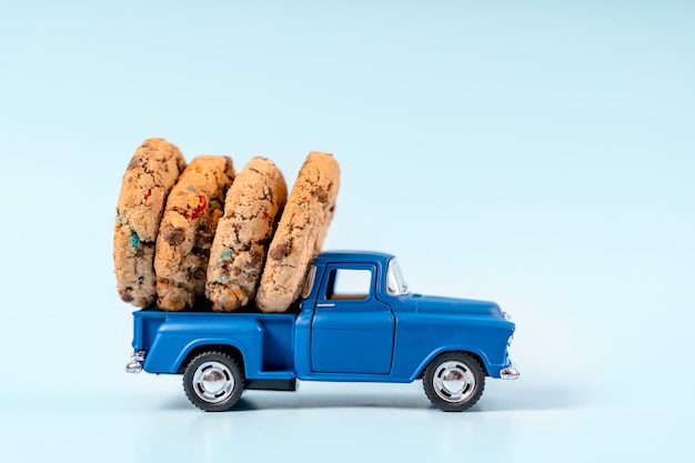 Een speelgoedauto vervoert koekjes met chocolade op een blauwe achtergrond Kerstkaart voor Nieuwjaar