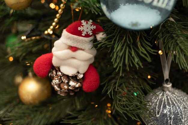 Een speelgoedkerstman op een kegel, hangend aan een kerstboom versierd met lichtjes van guirlandes