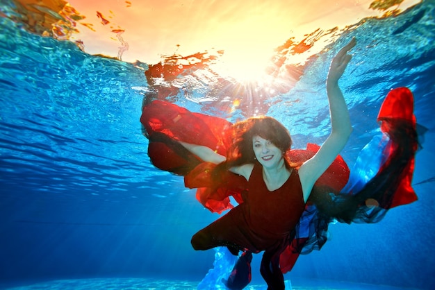 Een speels meisje met rood haar zwemt onder water in het zwembad met rode en blauwe stof