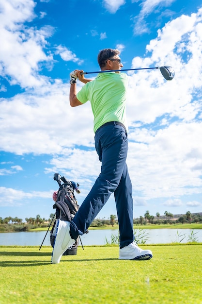 Een speler die golf speelt op de golfbaan die de bal raakt naast een verticale foto van een meer