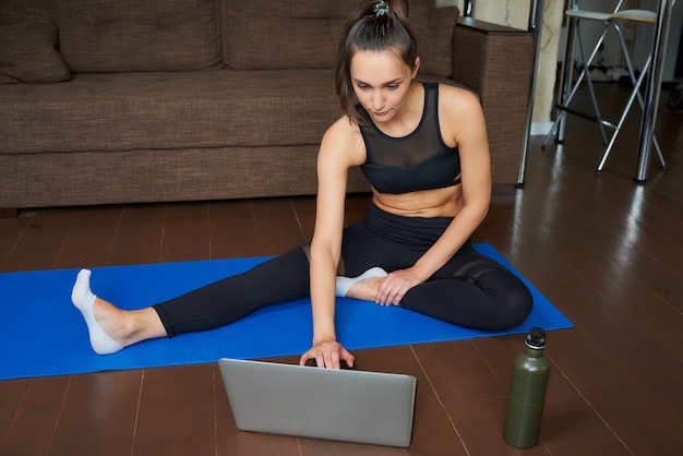 Een sportief meisje in een zwarte strakke broek en top doet een online workout