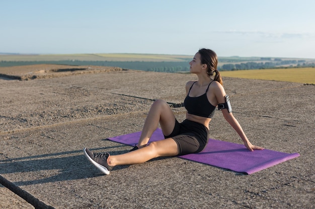 Een sportief slank meisje in legging en een top staat met een trainingsmat, rustend tussen de oefeningen.