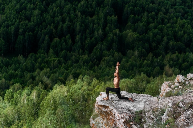 Een sportieve man doet yoga. Een gezonde leefstijl. De concentratie van het lichaam. Een man doet yoga in de bergen. Een man doet yoga op een rots. Een man mediteert in de natuur. Meditatie in de bergen