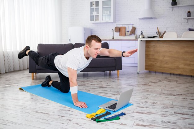 Een sportieve man in een T-shirt gaat thuis sporten in zijn ruime en lichte appartement met een minimalistisch interieur. internetsporten