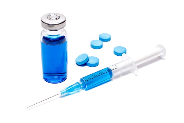 Een spuit met blauw vaccin en pillen