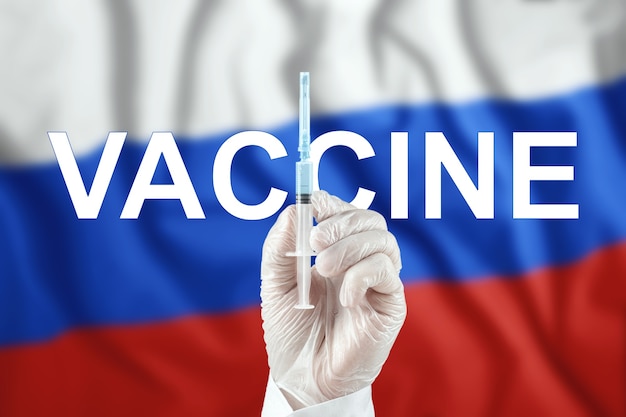 Een spuit met een vaccin in de hand van de dokter tegen de achtergrond van de russische vlag. covid-19-coronavirus, immuunbescherming, behandeling tegen ncov-infectie 2019, vaccinatie.