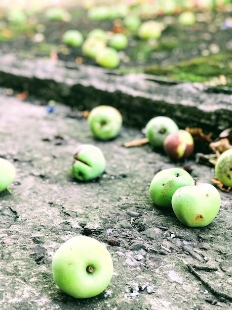 Een stapel appels op de grond met een groene appel op de grond.