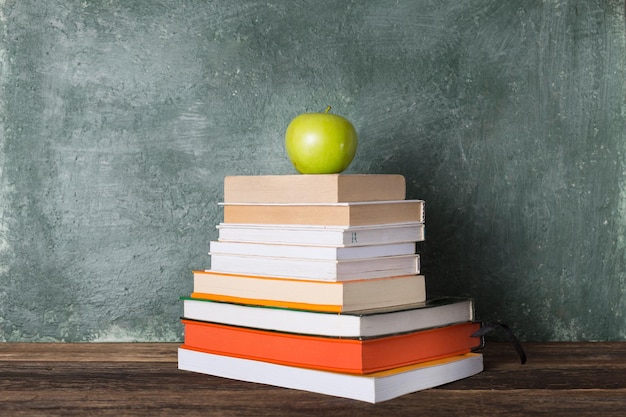 Een stapel boeken en een groene appel op de achtergrond van het schoolbestuur. Onderwijs en terug naar school concept.