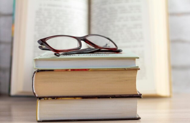 Een stapel boeken met een bril en een open boek op de achtergrond