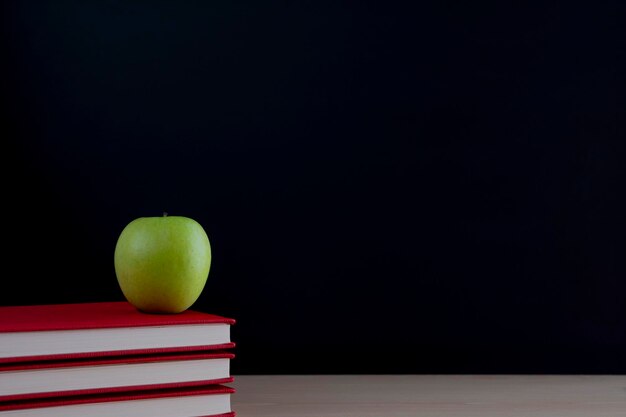 Een stapel boeken met een groene appel op het bureau op een zwarte achtergrond van het bord met een plaats voor de inscriptie